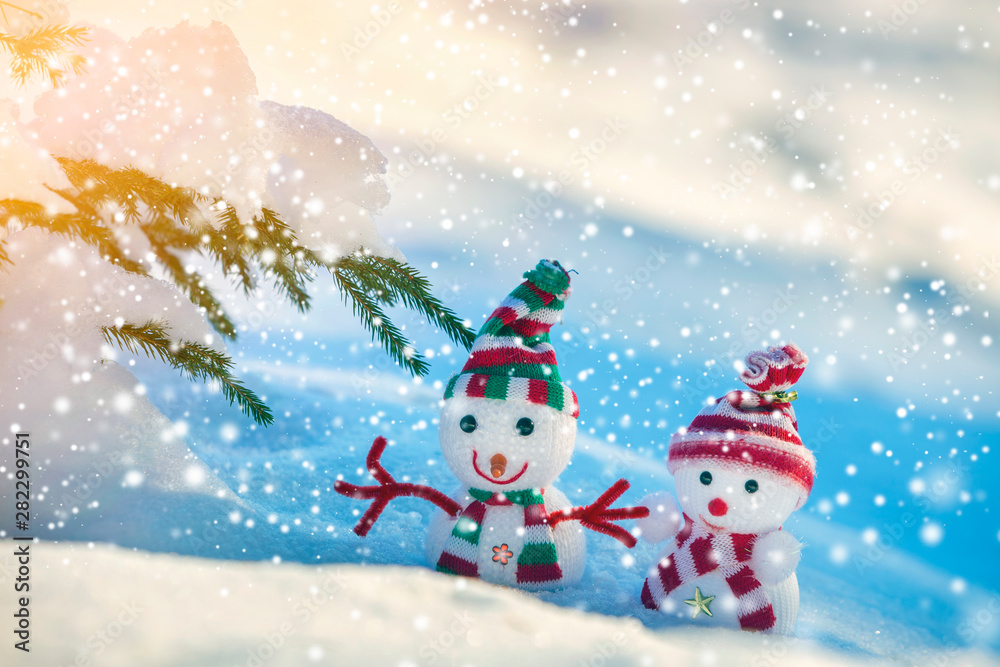 Two small funny toys baby snowman in knitted hats and scarves in deep snow outdoors on bright blue and white copy space background. Happy New Year and Merry Christmas greeting card. Two small funny toys baby snowman in knitted hats and scarves in deep snow outdoors on bright blue and white copy space background. Happy New Year and Merry Christmas greeting card.