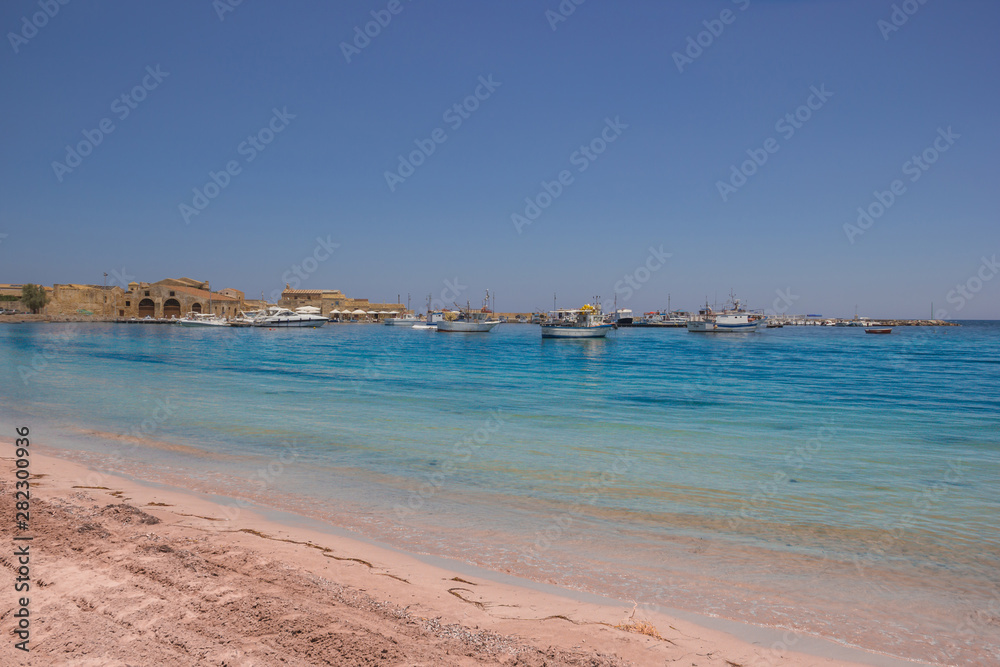 Marzamemi Sicily, beautiful beach and clear sea, with the historical village in background