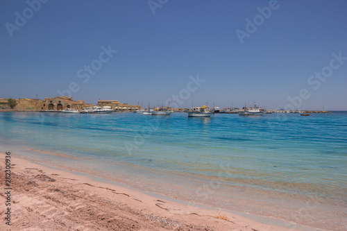 Marzamemi Sicily, beautiful beach and clear sea, with the historical village in background