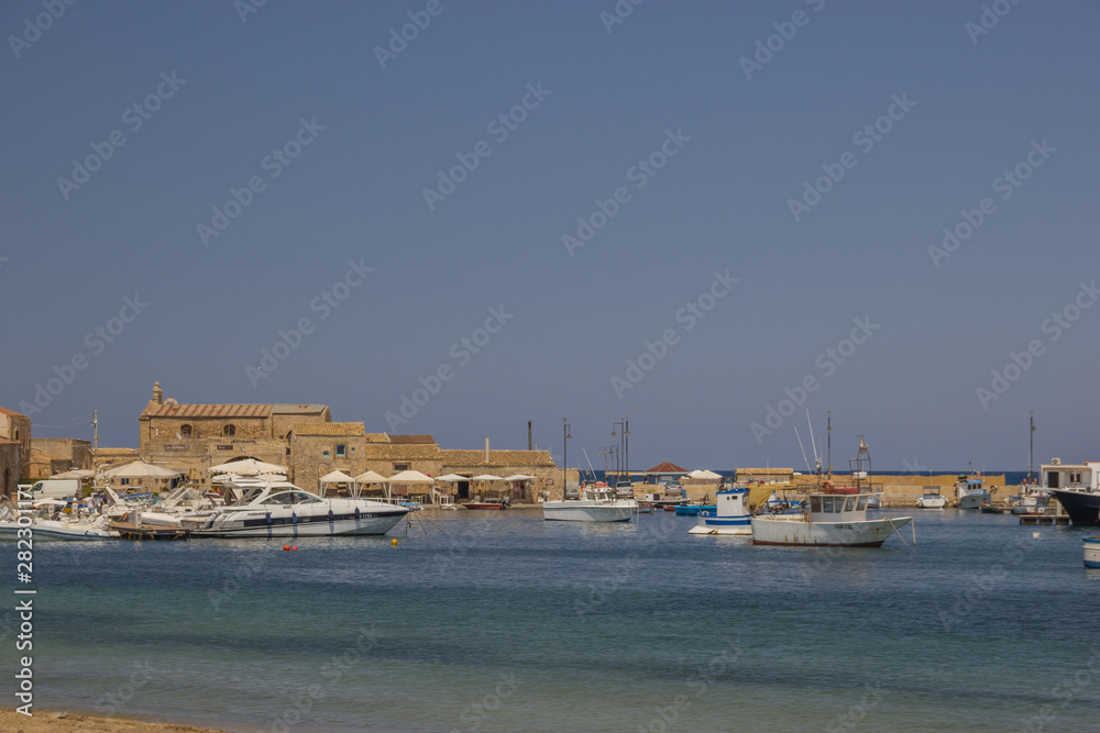 Marzamemi Sicily, view of the village from the beach and fishing port, view of old buildings, boats and beautiful sea