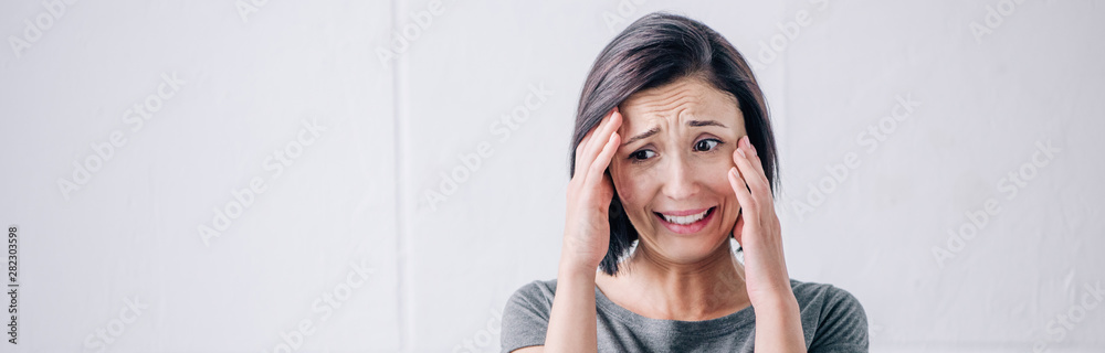 panoramic shot of depressed brunette woman touching face and crying at home panoramic shot of depressed brunette woman touching face and crying at home
