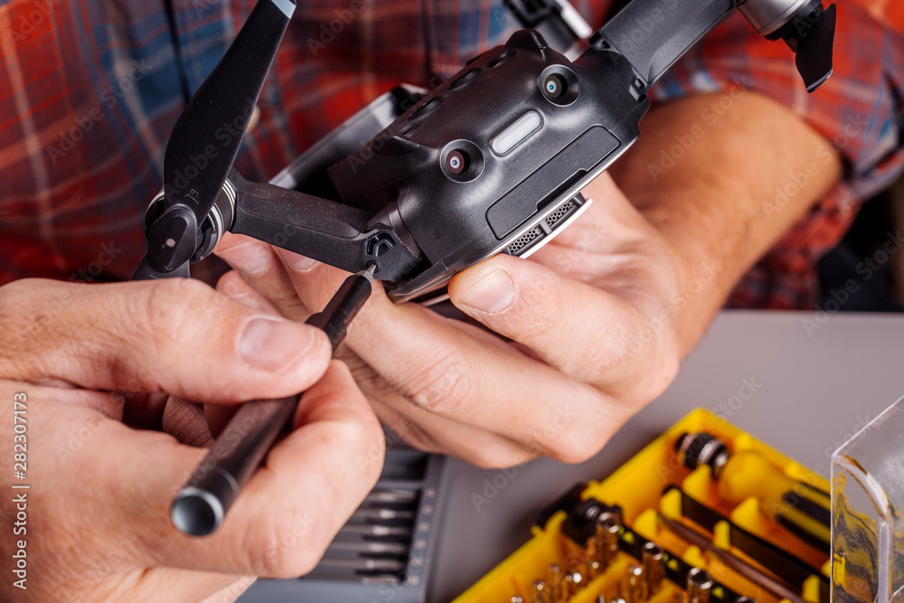 Man repairing quadcopter drone on table with different tools in modern workshop.