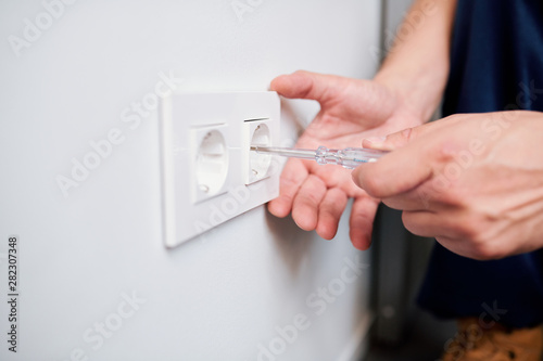 Hands of young professional electrician repairing or checking voltage of socket