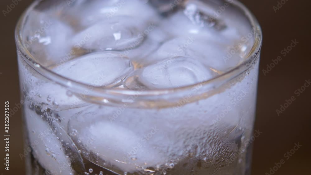 Macro Closeup Glass of cold refreshing fizzy drink with ice cubes. Soda with Ice in glass. Mineral bubbles. 360 rotation. 4K UHD video footage Macro Closeup Glass of cold refreshing fizzy drink with ice cubes. Soda with Ice in glass. Mineral bubbles. 360 rotation. 4K UHD video footage