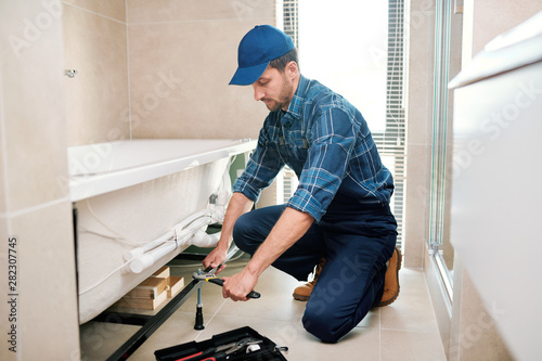 Young plumber or technician preparing detail for bathtub installation