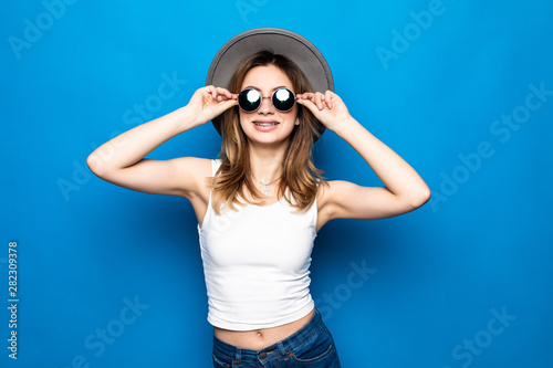 Fashion happy pretty smiling woman wearing a hat and sunglasses over colorful blue background