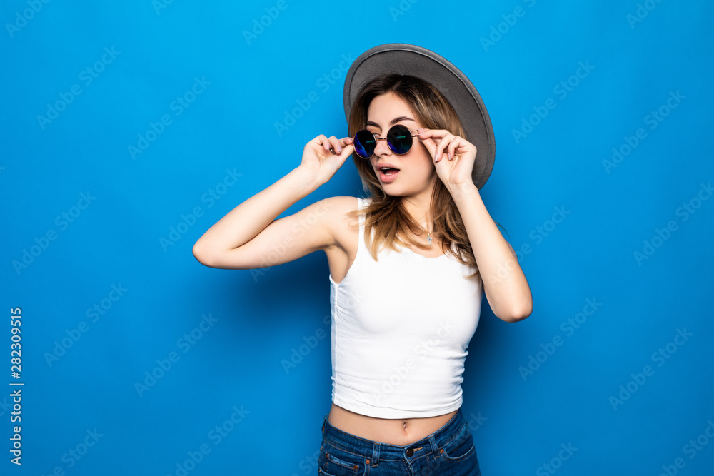 Portrait of pretty woman in sunglasses and hat over blue colorful background Portrait of pretty woman in sunglasses and hat over blue colorful background