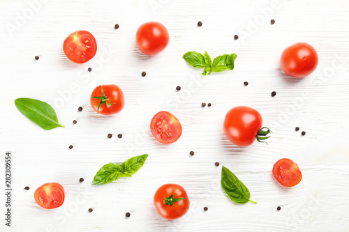 Bunch of juicy organic red cherry tomatoes arranged with green basil leaves on isolated white background. Polished vegetables. Clean eating concept. Vegetarian diet. Copy space, flat lay, top view.