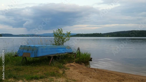 Blue fishing boat anchored on beach sand of lake. Smooth evening water level and calm. Large vallely of Lipno lake. photo