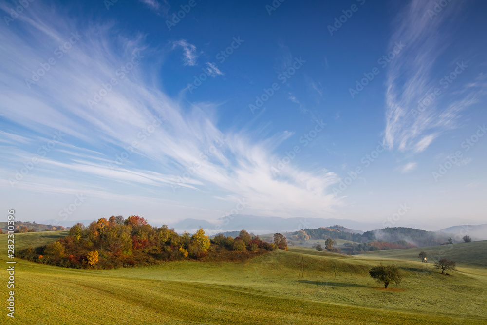 Fototapeta premium Fall in Slovakia. Meadows and fields landscape. Autumn color trees at sunrise.