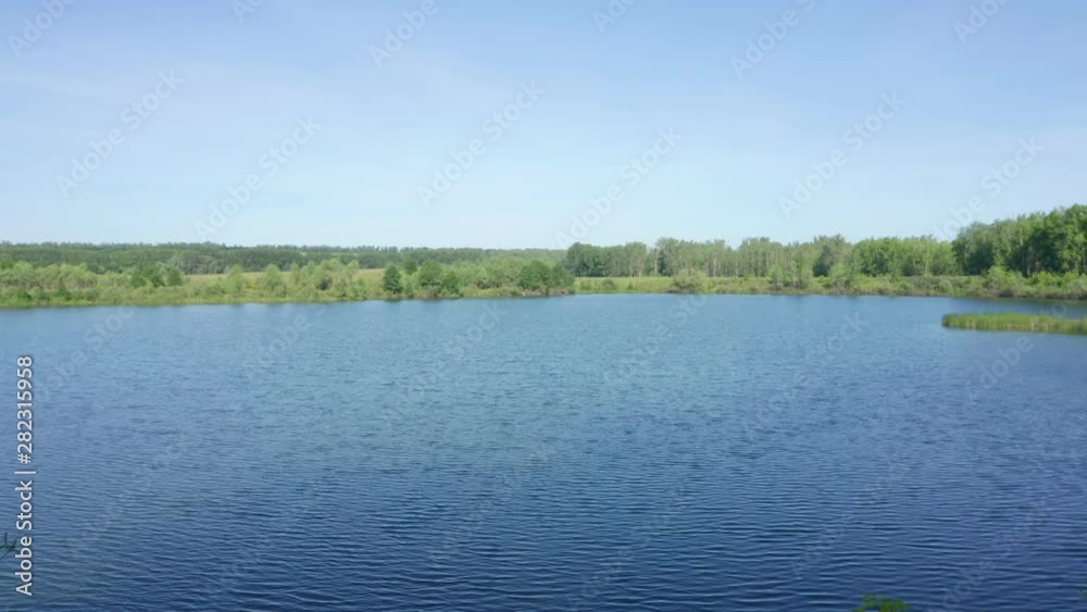 Aerial shot above the surface of the lake. Nice view of the lake. There are a lot of vegetation along the shores. Blue clear sky in the early morning. Aerial shot above the surface of the lake. Nice view of the lake. There are a lot of vegetation along the shores. Blue clear sky in the early morning.