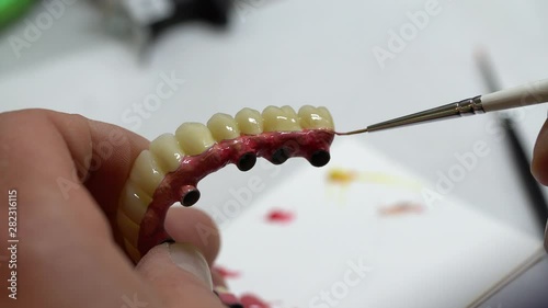 Skillful Dental Techician in Laboratory Applying Color to Zirconium Denture Prostethic, Close Up photo