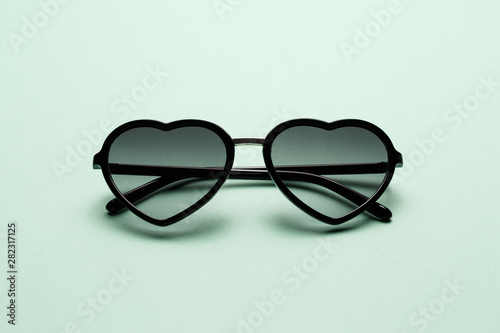 Fashionable sunglasses in shape of heart on mint background. Top view. Flat lay. Minimal style with colorful paper backdrop. The concept of summer, love and relaxation. Fashion summer accessory