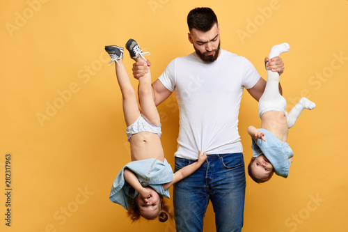Fotografie serious angry nervous sad young dad keeps his daughters' legs upside down