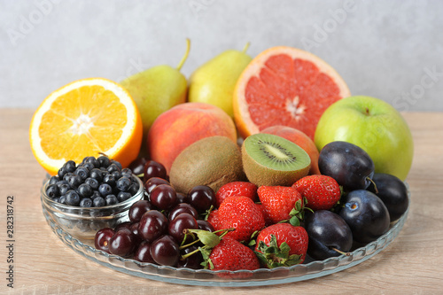 Acceptable fruits for diabetes. In a plate are orange  grapefruit  cherry  plum  pears  peaches  apple  plum  blueberries  kiwi. Light background. Close-up.