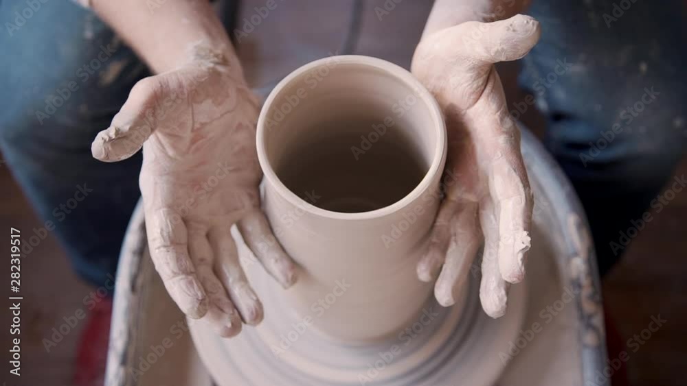 Hands of adult artisan people working with raw and wet clay. Busy man using electric wheel circle and making ceramic vase or potter in comfort workspace studio with soft light indoor Hands of adult artisan people working with raw and wet clay. Busy man using electric wheel circle and making ceramic vase or potter in comfort workspace studio with soft light indoor