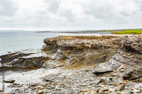 Limestone rocks with Doolin bay in the background in the coastal walk route from Doolin to the Cliffs of Moher, geosites and geopark, Wild Atlantic Way, spring day in county Clare in Ireland photo