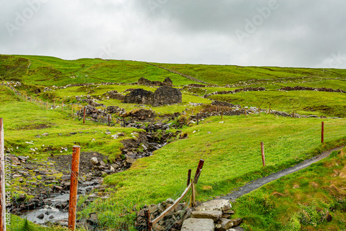 Ruined house next to a rill on the coastal route walk from Doolin to the Cliffs of Moher, geosites and geopark, Wild Atlantic Way, rainy day in in the countryside in county Clare in Ireland photo