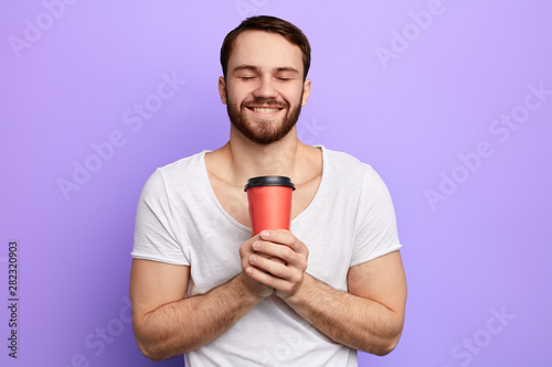 pleasant man drinking his favourite coffee. close up portrait. isolated blue background, studio shot. happiness, breakfast, free time, spare time