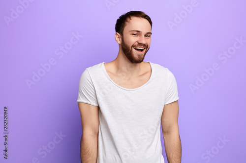 smiling, laughing young man with white t-shirt looking at the camera. isolated blue background. stduio shot. happiness, emotion and feeling, facial expression photo