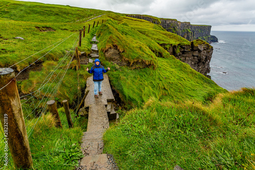 Irish landscape with cliffs and sea in background, female hiker on a bridge and stone coastal hiking trail from Doolin to Cliffs of Moher, rainy day in County Clare, Ireland. Wild Atlantic Way photo