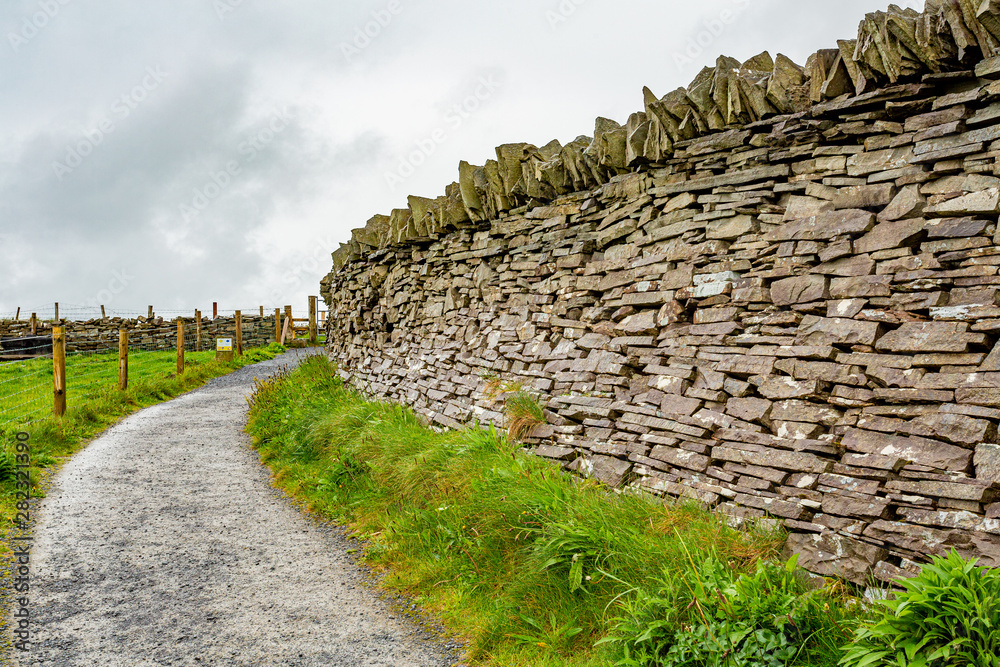 Natural limestone wall next to a path with fence of wooden poles and wire in the Burren, geosites and geopark, spring day in the countryside in County Clare in Ireland