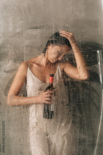 depressed woman in shower holding wine bottle and crying at home