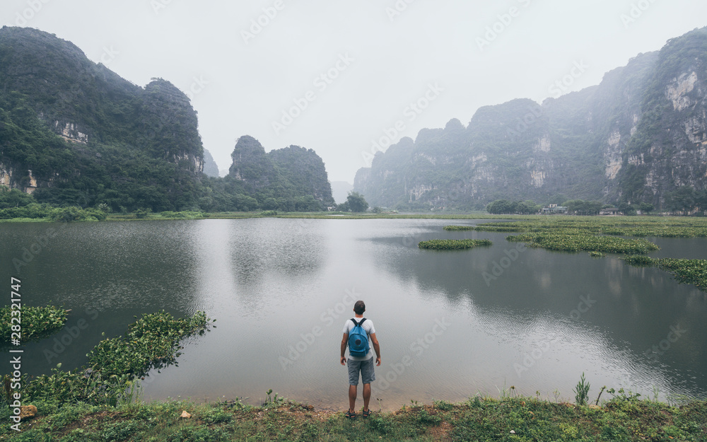 Caucasian man overlooking limestone mountains in Ninh Binh province, Vietnam. Cloudy day