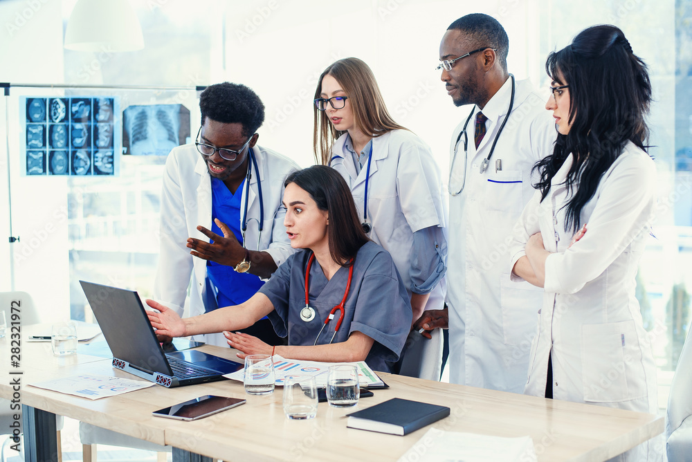 Group of multi national doctors using laptop for discussing analysis in the conference room. Side view. Group of multi national doctors using laptop for discussing analysis in the conference room. Side view.