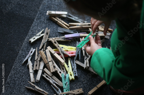 Details with the hands of a little girl playing with plastic and wooden clothes pegs on a wire photo