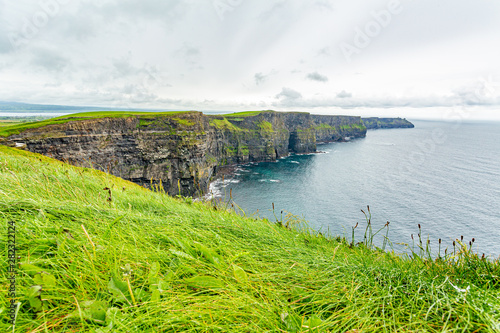 View of the Cliffs of Moher from a hill, geosites and geopark, Wild Atlantic Way, wonderful cloudy spring day in the countryside in county Clare in Ireland