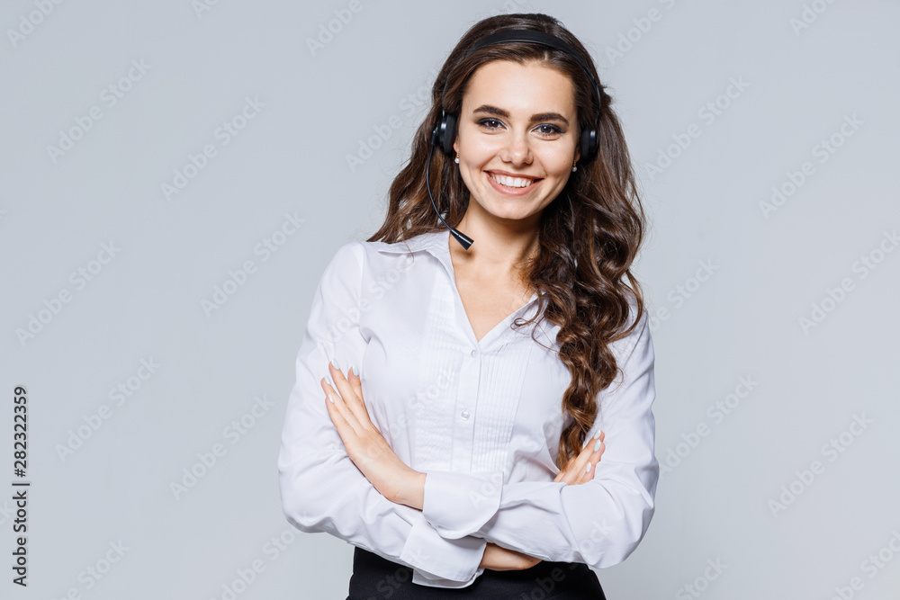 Young friendly operator woman agent with headsets standing near gray background. Call Center Service. Photo of customer support or sales agent in smart casual wear with crossed arms. Young friendly operator woman agent with headsets standing near gray background. Call Center Service. Photo of customer support or sales agent in smart casual wear with crossed arms.