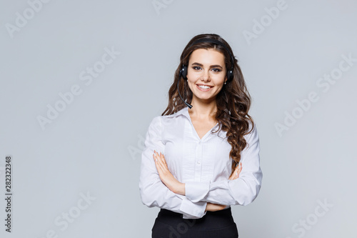 Young friendly operator woman agent with headsets standing near gray background. Call Center Service. Photo of customer support or sales agent in smart casual wear with crossed arms. photo
