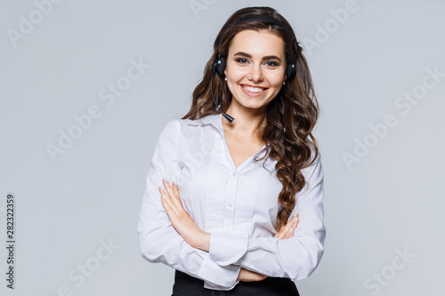 Young friendly operator woman agent with headsets standing near gray background. Call Center Service. Photo of customer support or sales agent in smart casual wear with crossed arms. photo