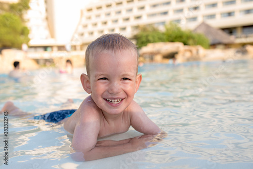 Adorable smiling boy looking at camera while having fun in outdoor swimming pool