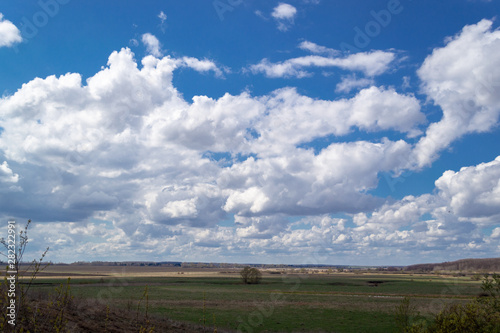 Massive cumulus white clouds in a blue sky over a green plain.