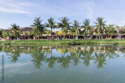 Hoi An, Vietnam - June 2019: reflection of palm trees, houses and boats in the river water