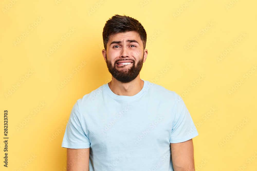 Puzzled confused crying poor man dressed casually looking at camera with thoughtful expression, biting his lip, being depressed before exams. isolated yellow background, studio shot Puzzled confused crying poor man dressed casually looking at camera with thoughtful expression, biting his lip, being depressed before exams. isolated yellow background, studio shot