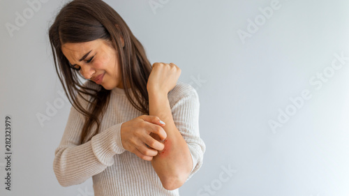 Young woman scratching arm from having itching on white background. Cause of itchy skin include insect bites, dermatitis, food/drugs allergies or dry skin. Health care concept. Close up.