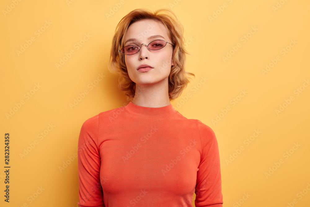 beautiful serious girl with pink glasses looking at the camera, fashion and beauty concept.isolated yellow background beautiful serious girl with pink glasses looking at the camera, fashion and beauty concept.isolated yellow background
