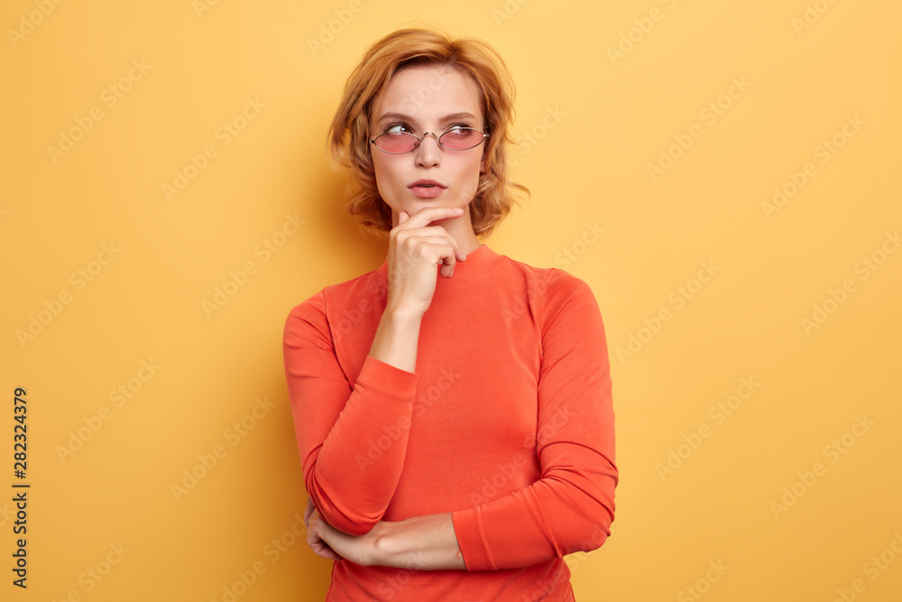 Beautiful young girl htful with hand on chin thinking about question, pensive expression.girl trying to solve a problem. isolated yellow background Beautiful young girl htful with hand on chin thinking about question, pensive expression.girl trying to solve a problem. isolated yellow background
