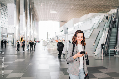 Young girl at the airport walks, looking down at her smartphone smiling.
