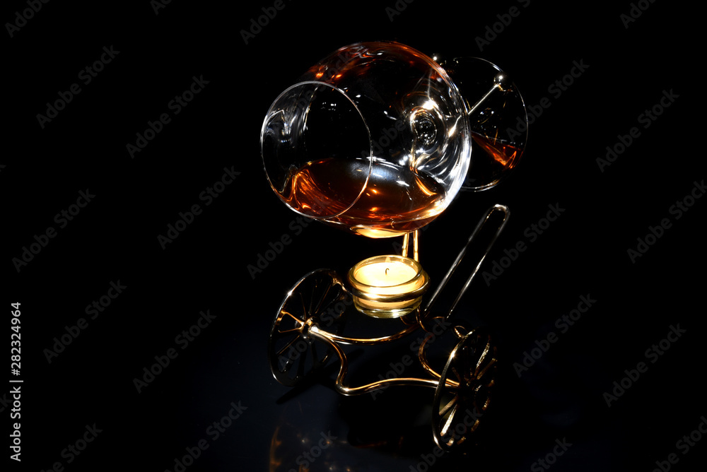 A glass of cognac on a special stand with candle for warming drink in the dark A glass of cognac on a special stand with candle for warming drink in the dark