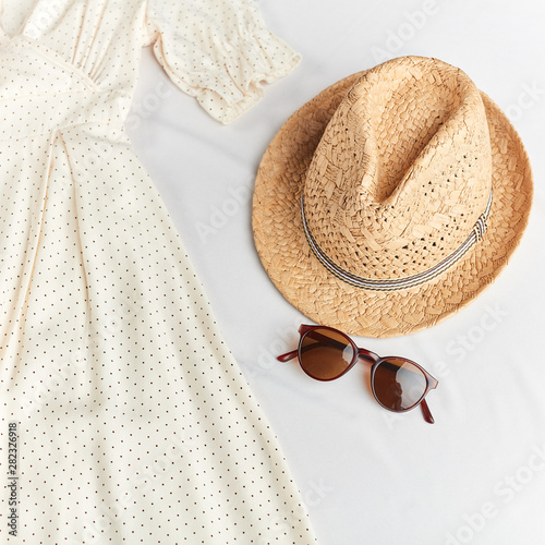 straw stylish hat  sunglasses and polka dot white dress on white background. top view photo. girl has taken off clothes and gone to swim
