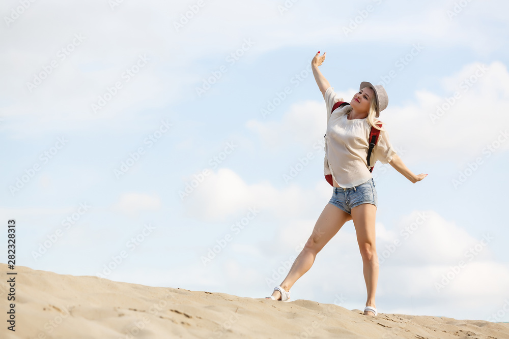 stylish beautiful smiling cheerful woman running happy in desert sand dressed in white trousers and blouse wearing straw hat on sunset, travel safari on vacation, sunny summer day