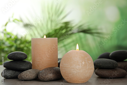 Burning candles and spa stones on table against blurred green background