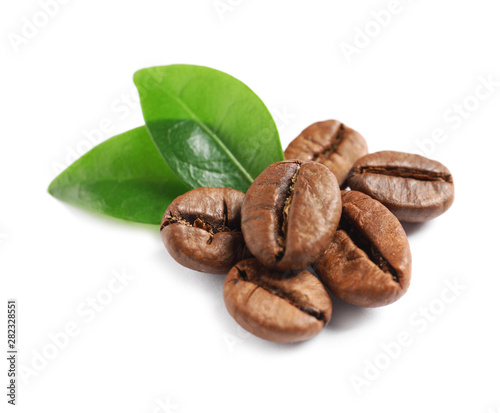 Roasted coffee beans and fresh green leaves on white background