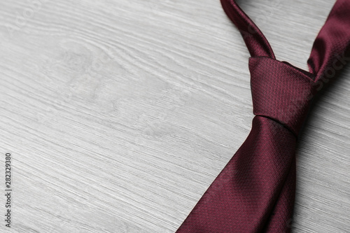 Stylish bordeaux necktie on grey wooden table, space for text