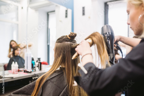 Portrait of happy woman at the hair salon. Professional hair styling concept. Hairdresser drying girl long hair using hairdryer and brush. Drying With Blow Dryer