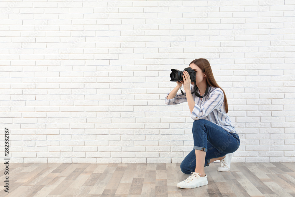 Professional photographer taking picture near white brick wall. Space for text - obrazy, fototapety, plakaty 